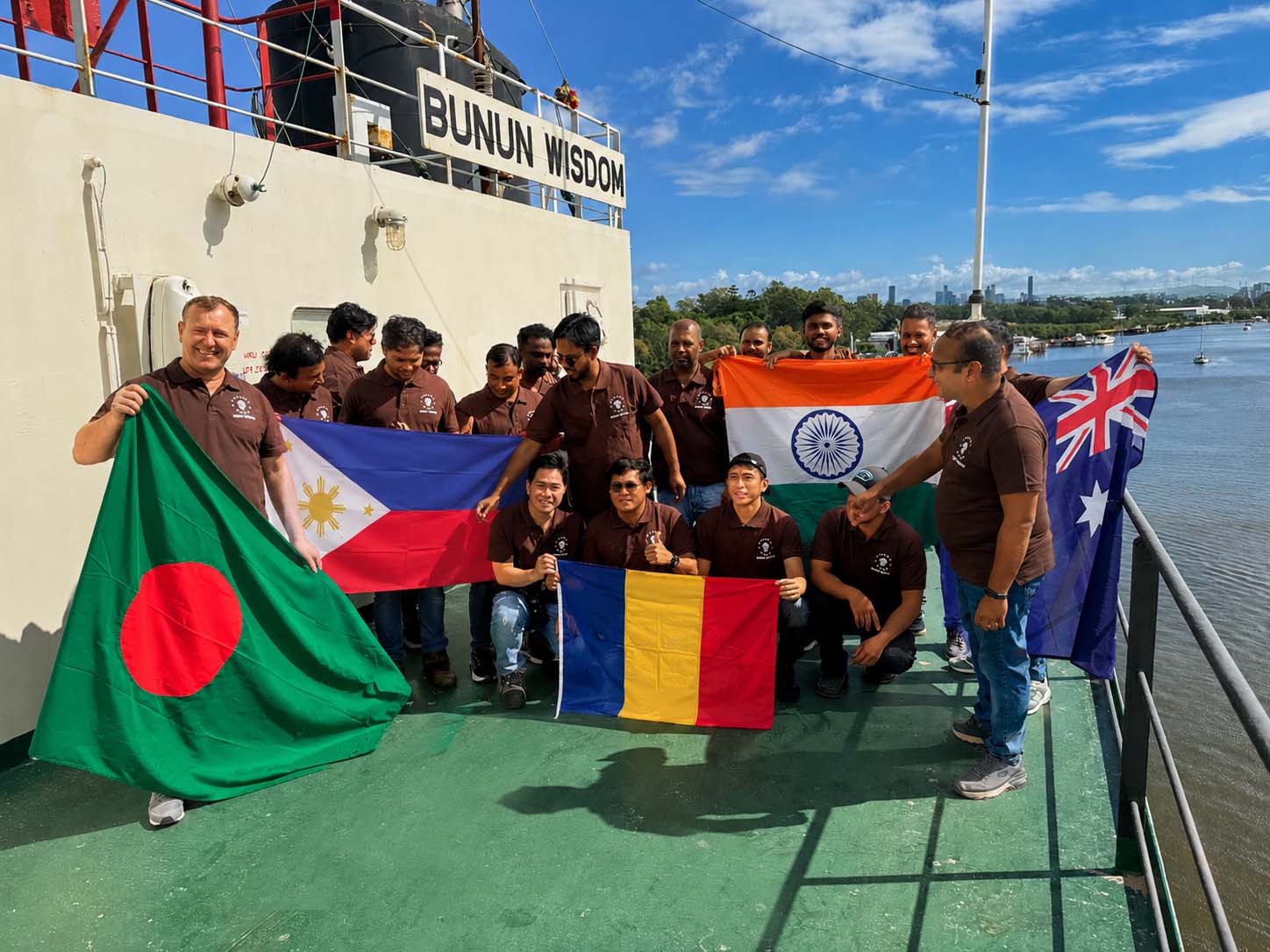 Multinational ship crew holding national flags on the deck of the vessel Bunun Wisdom, representing Synergy Marine Group crew management services.